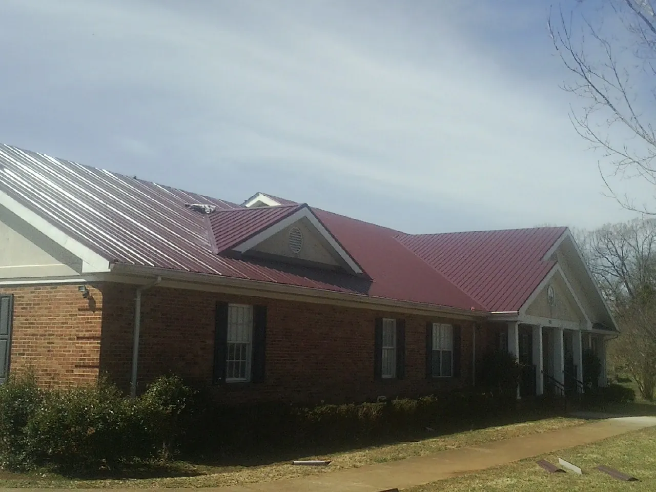 Red metal roof with gabled entries on a long brick building, from a Hail Damage Roof Repair job in Logan