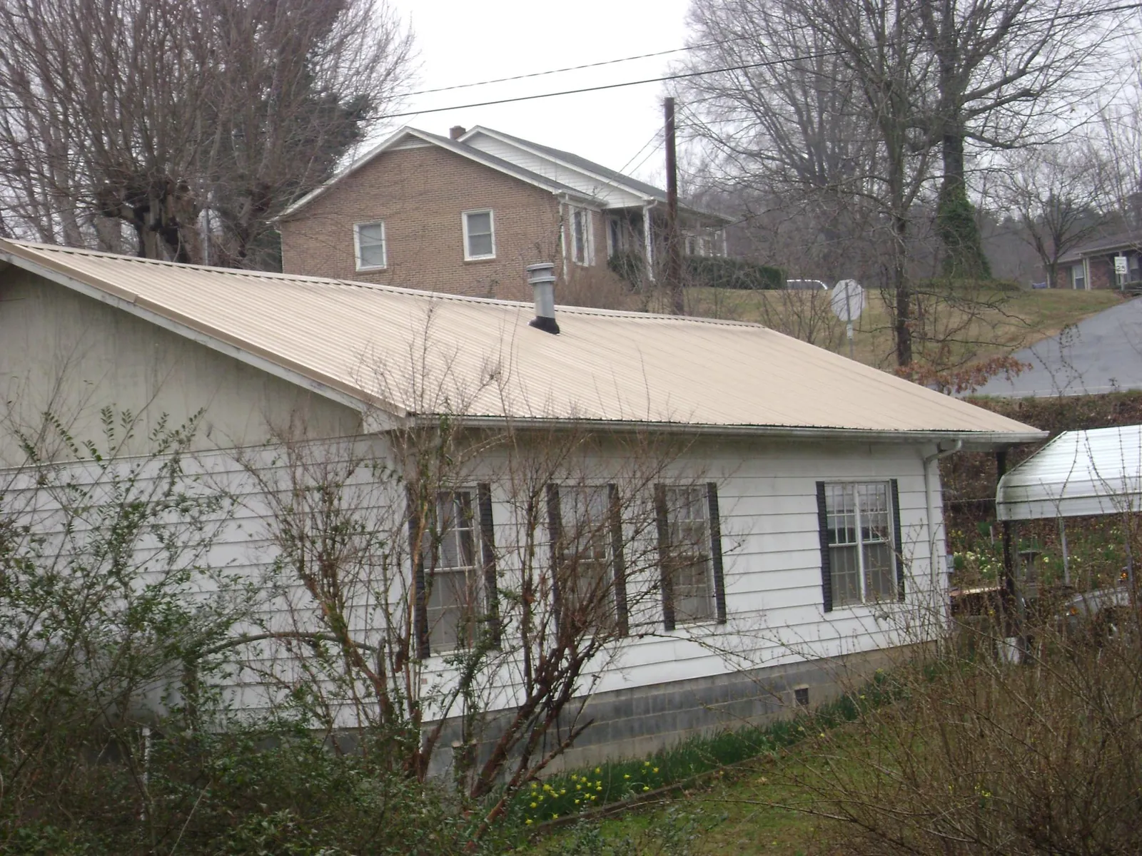 Tan metal roof on a white sided house set into a hillside — Commercial Roofing by Roofing Brothers in Logan